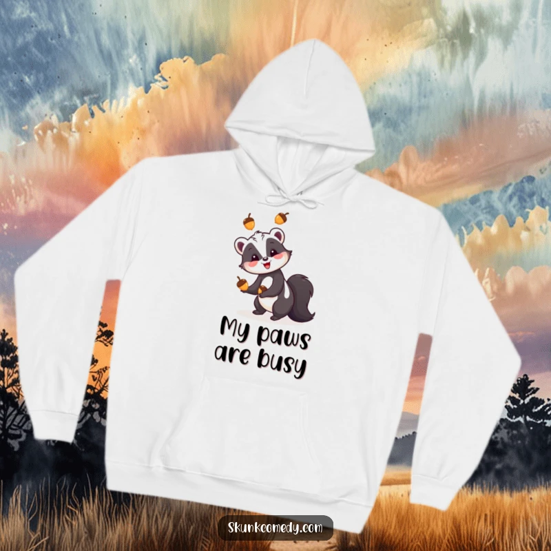Funny skunk hoodie, a skunk happily juggling three colorful acorns, cozy and whimsical outdoor-themed apparel.